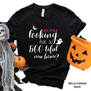 May include: Black Bella Canvas t-shirt with the text "looking for a BOO-tiful new home?" in white script, with a ghost graphic. The RE/MAX logo is in red and blue. A Halloween-themed shirt.