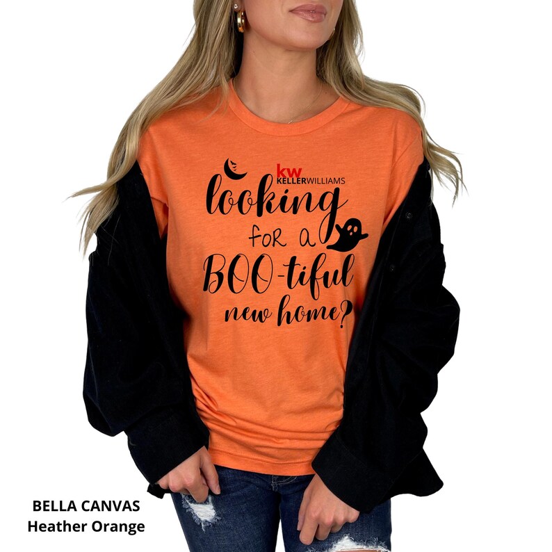 May include: A heather orange short-sleeve t-shirt featuring black text that reads "looking for a BOO-tiful new home?" with a small black crescent moon and ghost graphic. Above the text is the red and black "KW KELLERWILLIAMS" logo.