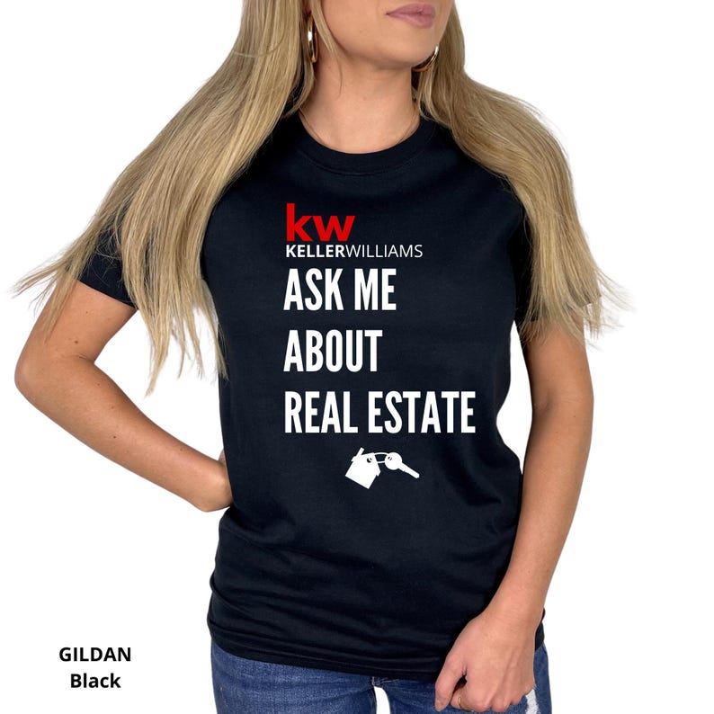 May include: Black t-shirt with the Keller Williams logo in red and the text "ASK ME ABOUT REAL ESTATE" in white. A graphic of a house and key is below the text. The shirt is a Gildan brand.