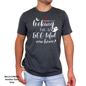 May include: A heather dark grey short-sleeve t-shirt featuring white text that reads "looking for a BOO-tiful new home?" with a small white crescent moon and ghost graphic, plus the red and white "KW KELLERWILLIAMS" logo printed on the chest.