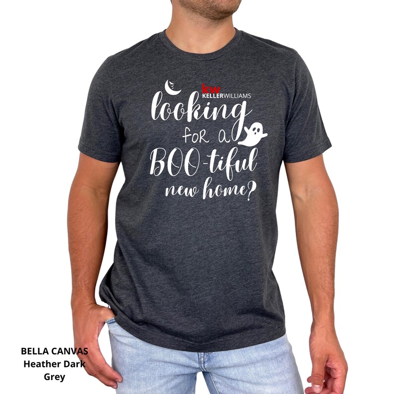 May include: A heather dark grey short-sleeve t-shirt featuring white text that reads "looking for a BOO-tiful new home?" with a small white crescent moon and ghost graphic, plus the red and white "KW KELLERWILLIAMS" logo printed on the chest.