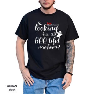 May include: A black short-sleeved t-shirt featuring white text that reads "looking for a BOO-tiful new home?" along with a small white ghost icon, a crescent moon, and the red and white "KW KELLERWILLIAMS" logo printed on the chest area.