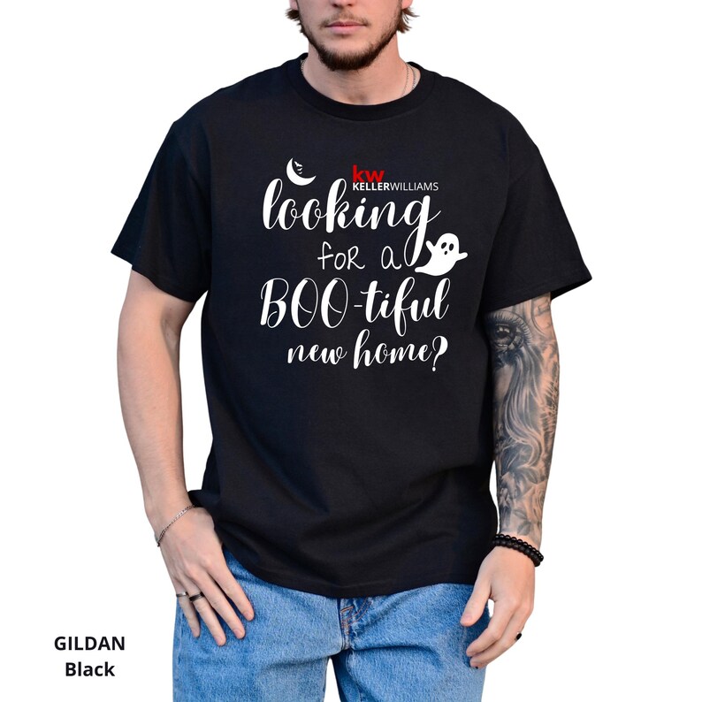 May include: A black short-sleeved t-shirt featuring white text that reads "looking for a BOO-tiful new home?" along with a small white ghost icon, a crescent moon, and the red and white "KW KELLERWILLIAMS" logo printed on the chest area.