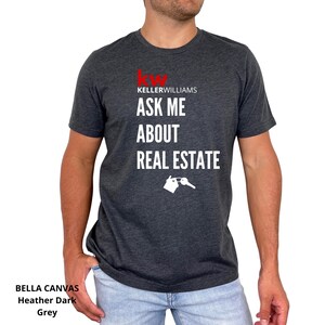 May include: Dark grey Bella Canvas t-shirt with the Keller Williams logo in red. The shirt features the text "ASK ME ABOUT REAL ESTATE" in white, along with a house and key graphic. The shirt is heather dark grey.
