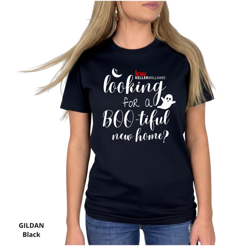 May include: A black short-sleeved t-shirt featuring white text that reads "looking for a BOO-tiful new home?" with a small white crescent moon, a ghost graphic, and the red and white Keller Williams logo printed on the front chest area.