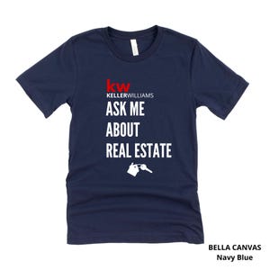 May include: Navy blue Bella Canvas t-shirt with the text "Ask Me About Real Estate" in white. The Keller Williams logo is in red. A graphic of a house and key is below the text. The shirt is navy blue.