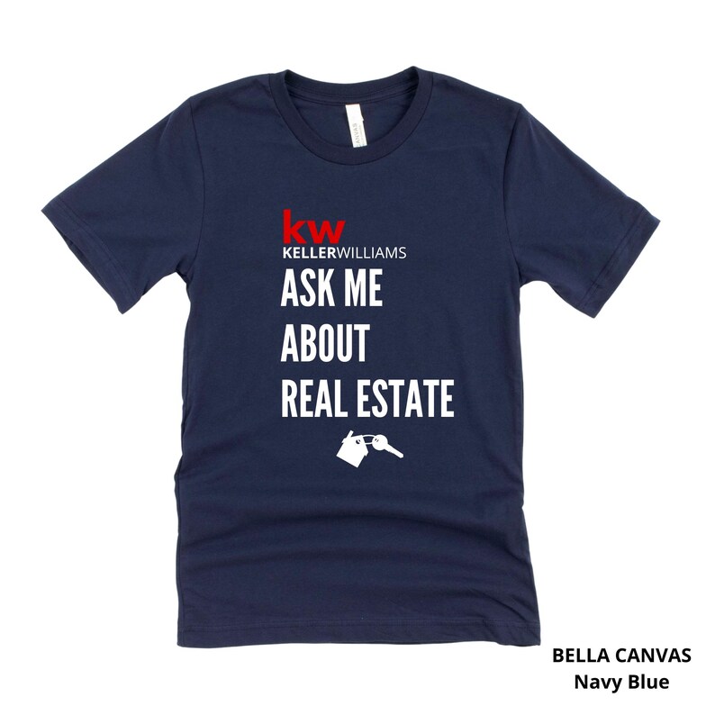 May include: Navy blue Bella Canvas t-shirt with the text "Ask Me About Real Estate" in white. The Keller Williams logo is in red. A graphic of a house and key is below the text. The shirt is navy blue.