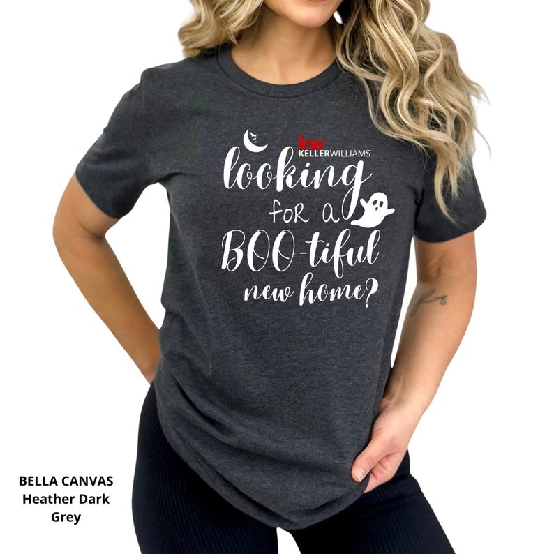 May include: A heather dark grey short-sleeve t-shirt featuring white text that reads "looking for a BOO-tiful new home?" with a small white ghost and crescent moon graphic, plus the red and white "KELLERWILLIAMS" logo printed on the chest.