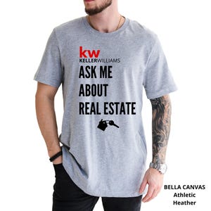 May include: Athletic heather gray t-shirt with the Keller Williams logo and the text "ASK ME ABOUT REAL ESTATE". The design includes a house and key graphic. The shirt is made of Bella Canvas material.