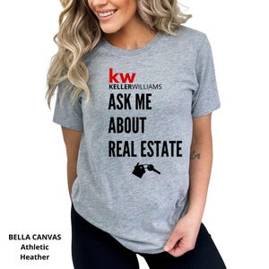 May include: Athletic heather gray t-shirt with the Keller Williams logo and the text "ASK ME ABOUT REAL ESTATE". The design includes a house and key graphic. The shirt is made of Bella Canvas material.