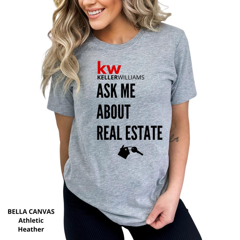 May include: Athletic heather gray t-shirt with the Keller Williams logo and the text "ASK ME ABOUT REAL ESTATE". The design includes a house and key graphic. The shirt is made of Bella Canvas material.