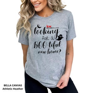 May include: A heather gray short-sleeve t-shirt featuring black text that reads looking for a BOO-tiful new home? with a small black crescent moon and ghost graphic. The shirt also includes the red and black Keller Williams logo text.