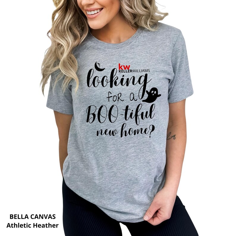 May include: A heather gray short-sleeve t-shirt featuring black text that reads looking for a BOO-tiful new home? with a small black crescent moon and ghost graphic. The shirt also includes the red and black Keller Williams logo text.