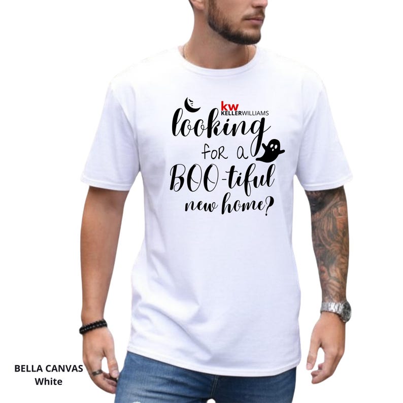 May include: A white short-sleeve t-shirt featuring black cursive text that reads looking for a BOO-tiful new home? with a small black ghost icon and the red and black Keller Williams logo printed on the front chest area of the garment.