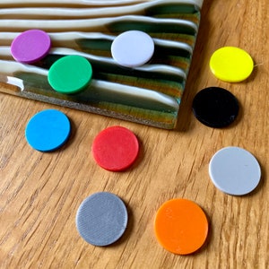 Puede incluir: Surtido de diez piezas redondas de juego de colores en varios colores, incluyendo rojo, azul, verde, amarillo, blanco, negro y gris. Las piezas son de plástico y tienen un diámetro de aproximadamente 2,5 cm.