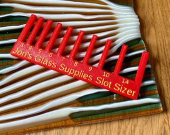 Może przedstawiać: Czerwone plastikowe narzędzie z grzebieniowym wzorem i numerowanymi szczelinami od 3 do 14. Narzędzie jest oznaczone jako "Jon's Glass Supplies Slot Sizer".