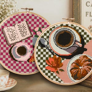 May include: Two cross-stitch hoops with coffee and book designs. One features a cup of coffee and a croissant, the other a cup and a book. The background is a checkered pattern in pink and green.