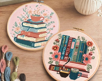 May include: Two circular wooden embroidery hoops containing cross-stitch designs on light pink fabric. One hoop features a stack of books topped with a steaming mug and flowers. The other hoop displays upright books, including one labeled Book Club, with flowers and mugs.