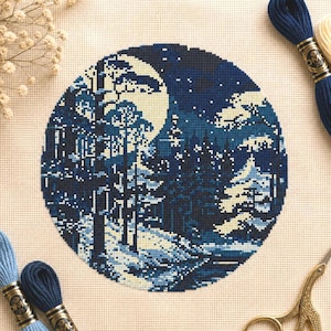 May include: A round cross-stitch design depicting a moonlit forest scene in shades of blue and white. The design features trees, a full moon, and a starry sky. Embroidery floss and scissors are visible around the design.