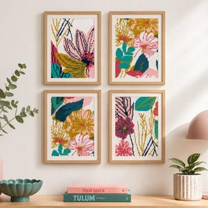 Op de afbeelding: Vier ingelijste bloemenkunstprints met een botanisch thema. Elke print heeft een kleurrijk abstract ontwerp met roze, gele, turquoise en witte bloemen en bladeren. De frames zijn gemaakt van lichtgekleurd hout en worden op een witte muur weergegeven.