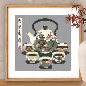 May include: Cross-stitch artwork in a wooden frame, depicting a teapot and teacups. The teapot is green with floral details, and the cups have different patterns. The background is grey, creating a cohesive and decorative piece.