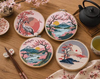 May include: Four circular wooden embroidery hoops featuring cross-stitch designs of Japanese landscapes. The patterns include a crane, Mount Fuji, cherry blossoms, and sun motifs in shades of pink, blue, white, and black on fabric.