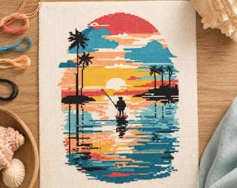 May include: Cross-stitch artwork showing a sunset scene with a fisherman on a boat. The design uses a vibrant colour palette of red, orange, yellow, and blue, with palm trees and clouds. The artwork is on a white canvas.