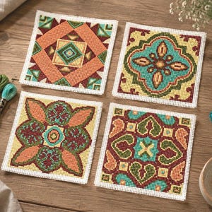 Könnte beinhalten: Vier quadratische Kreuzstich-Stickereien mit geometrischen und floralen Mustern in Orange-, Türkis-, Gelb- und Dunkelrottönen. Jedes Stück ist auf weißem Aida-Stoff gearbeitet und wird von mehreren bunten Stickgarnsträngen begleitet.