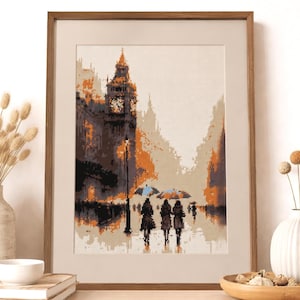 May include: Framed cross-stitch art depicting a rainy street scene in London. The artwork features Big Ben, figures with umbrellas, and a color palette of brown, orange, and gray. The piece is displayed in a wooden frame.
