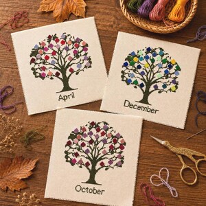 May include: Three square pieces of cream-colored Aida fabric featuring cross-stitch tree designs. Each tree has a dark green trunk and branches with colorful leaves. The labels April, December, and October are stitched below each respective tree.