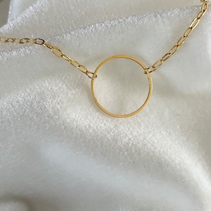 Puede incluir: Un collar de cadena de oro con un colgante circular simple.