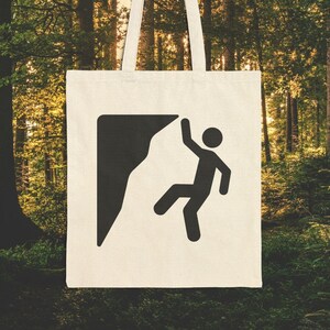May include: A white canvas tote bag with a black silhouette of a person climbing a rock face. The bag has two handles and is perfect for carrying everyday essentials.