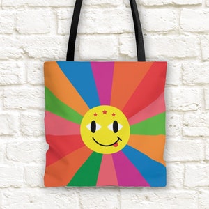 May include: A colorful tote bag with a rainbow design and a yellow smiley face with red stars and a tongue sticking out.