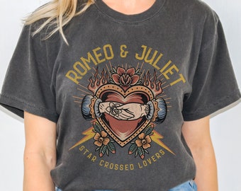 May include: A charcoal gray t-shirt with a graphic print of a heart with two hands clasped together. The text "Romeo & Juliet" is above the heart and "Star Crossed Lovers" is below the heart.