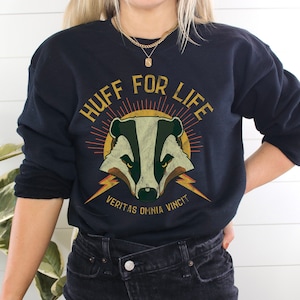 May include: Black sweatshirt with a vintage-style graphic of a badger with the text "HUFF FOR LIFE" and the Latin phrase "VERITAS OMNIA VINCIT" underneath.