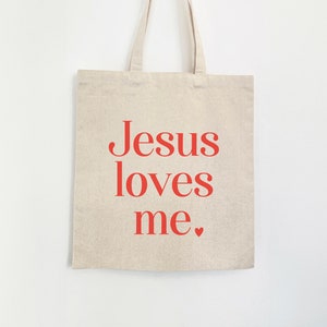 May include: A beige canvas tote bag with a red print that says "Jesus loves me."