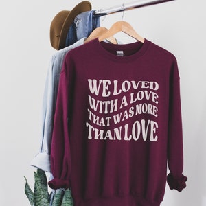 May include: Burgundy sweatshirt with white text that reads "We loved with a love that was more than love".