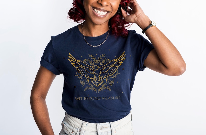 May include: A navy blue t-shirt with a gold outline of a bird in flight surrounded by floral designs and stars. The text "WIT BEYOND MEASURE" is printed below the bird.