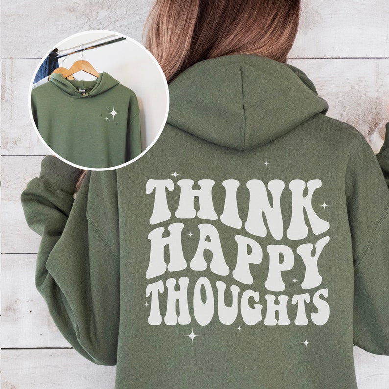 以下が含まれることがあります： 背面に白い文字で「Think Happy Thoughts」と書かれた緑色のフード付きスウェットシャツ。文字はレトロなフォントで、周りに白い星が散りばめられています。