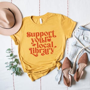 mustard yellow t shirt with red text support your local library