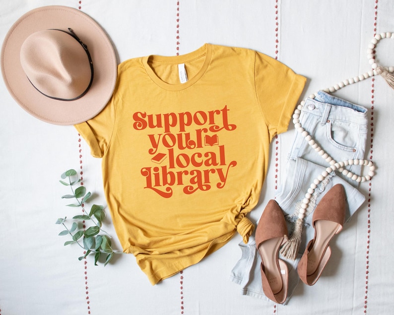 mustard yellow t shirt with red text support your local library