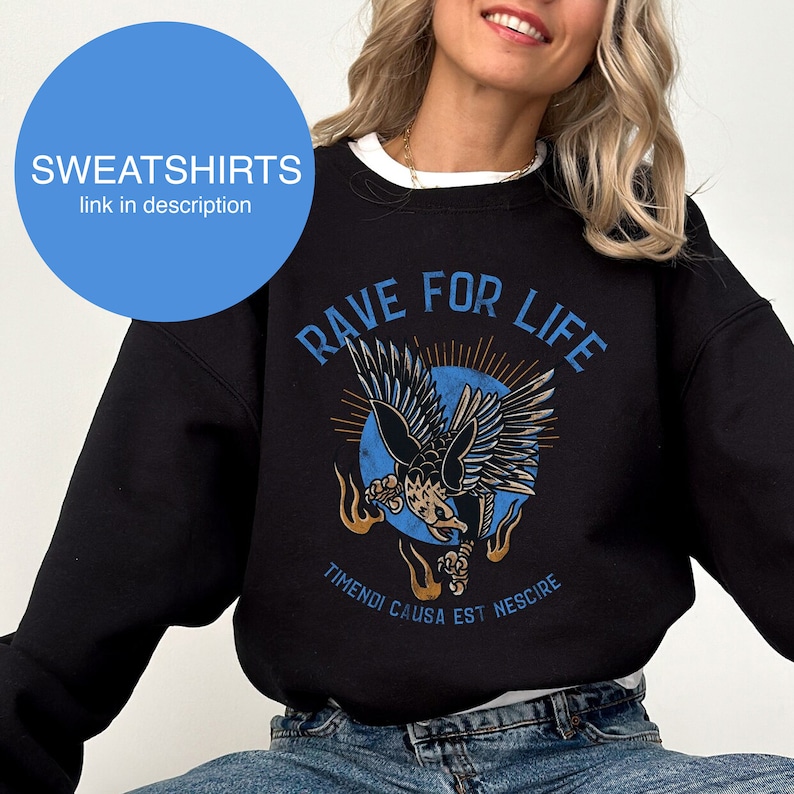 May include: Black sweatshirt with a blue and orange graphic of an eagle with the text "Rave For Life" and "Timendi Causa Est Nescire" below the graphic.