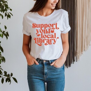 white t shirt with red text support your local library