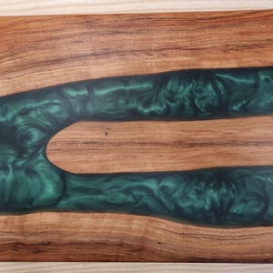May include: Wooden serving tray with a rich, natural wood grain and a vibrant, emerald green epoxy resin river design. Features black metal handles on each end for easy carrying. A decorative and functional piece.