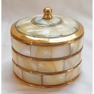 May include: A round, white and gold decorative box with a lid. The box is made of mother of pearl tiles and has a gold trim around the edges. The lid has a small gold knob on top.