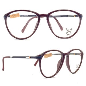 May include: Round, burgundy-colored eyeglasses with a dark navy blue accent on the frame. The Playboy logo is visible on the right lens. The glasses have a price tag attached.