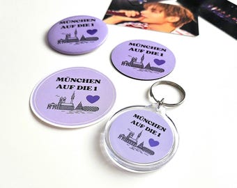 Conjunto de produtos BTS "Munich on the 1" com 4 peças: botão, chaveiro, ímã e adesivo.