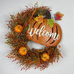 May include: A fall-themed wreath with a metal pumpkin that says "Welcome" in white lettering. The wreath is decorated with faux fall leaves and small orange pumpkins.