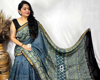 May include: A blue saree featuring a repeating geometric and floral pattern in light green and gold. The fabric has a dark gold border and a solid black section at the end. The number 9 is printed in white on the fabric of the draped garment.