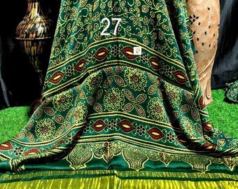 Op de afbeelding: Een groene stof met een herhalend goud en bordeauxrood bloemen- en paisleypatroon met het cijfer 27 in het midden gedrukt. Het onderste gedeelte toont horizontale gouden en zwarte strepen met een effen zwarte rand aan de onderkant.